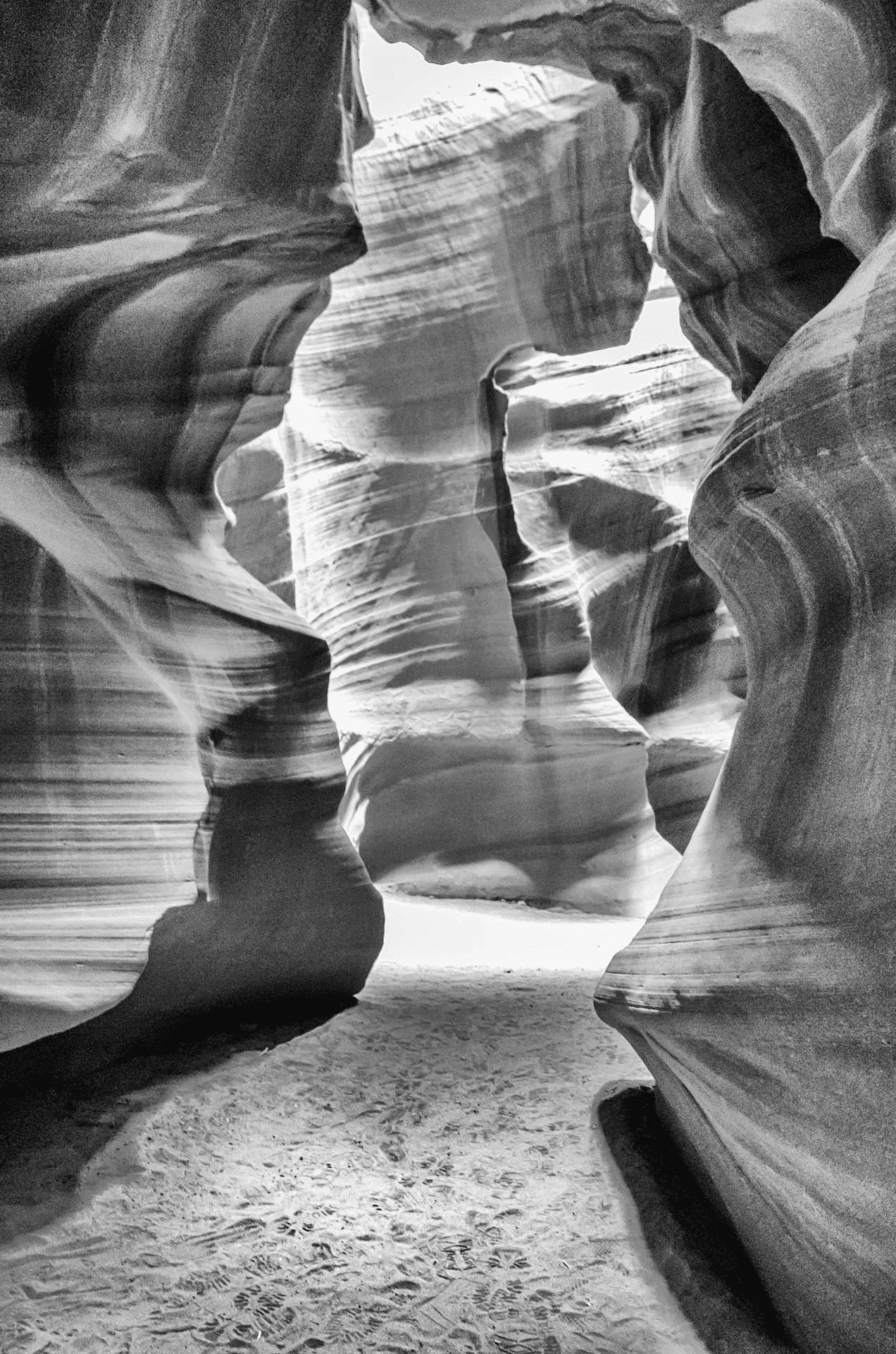Black and white landscape photograph of Antelope Canyon, Arizona. The image captures the interior of a slot canyon, showcasing the wavy, sculpted sandstone walls in shades of grey.