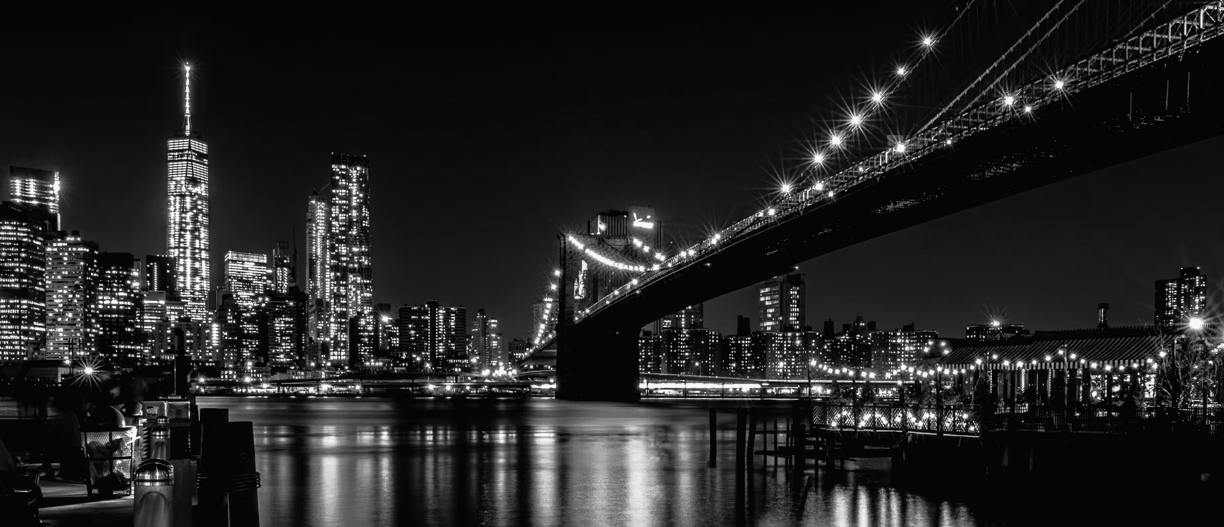 Monochrome cityscape featuring the Brooklyn Bridge's Gothic Revival architecture illuminated against the Manhattan skyline.