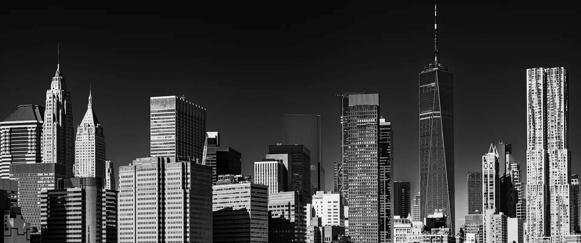 A striking black and white photograph of the New York City skyline, featuring a dense cluster of skyscrapers against a stark, clear sky.