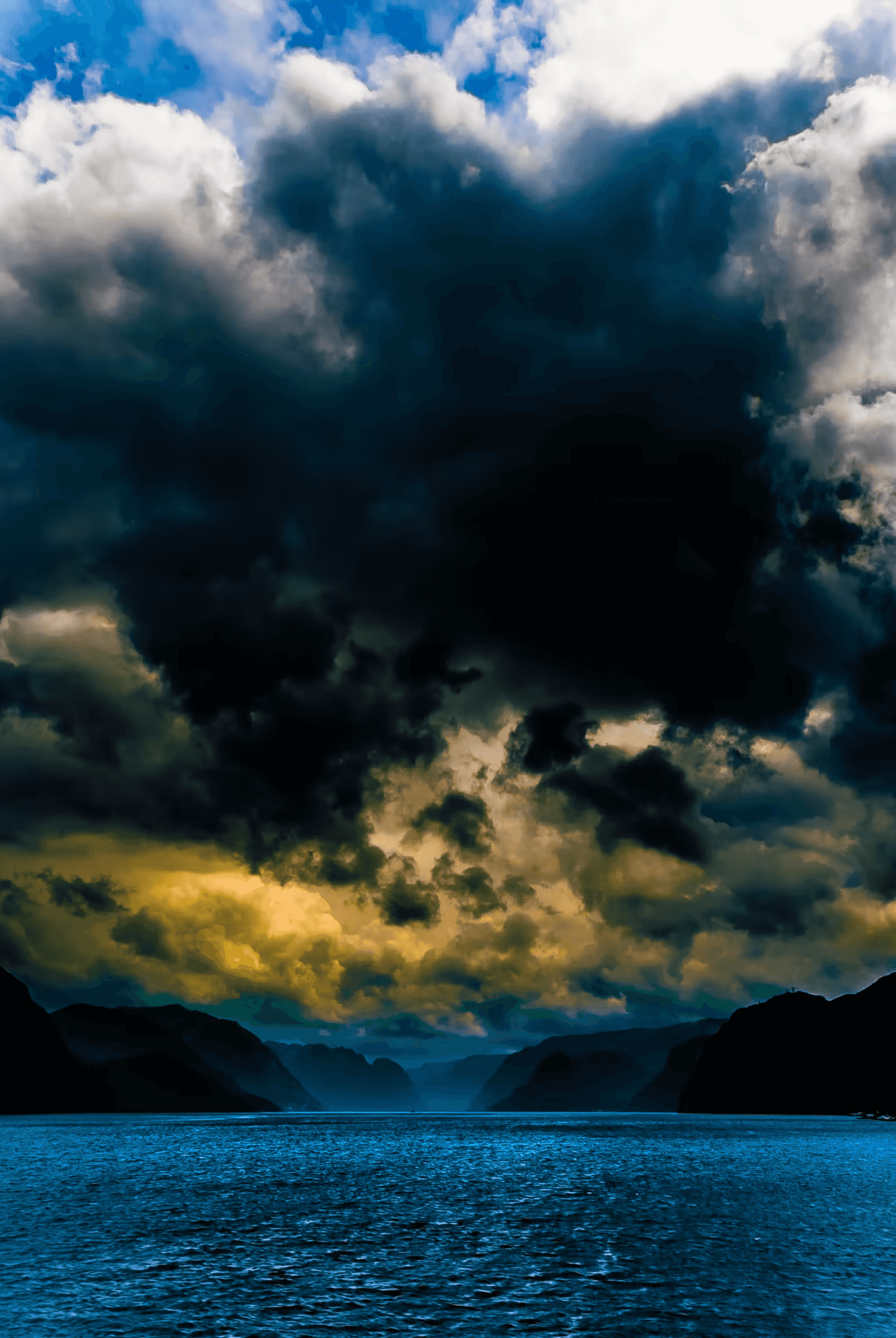 Norwegian fjord landscape showing heavy storm clouds reflected in calm water, with distant mountain silhouettes creating atmospheric depth.