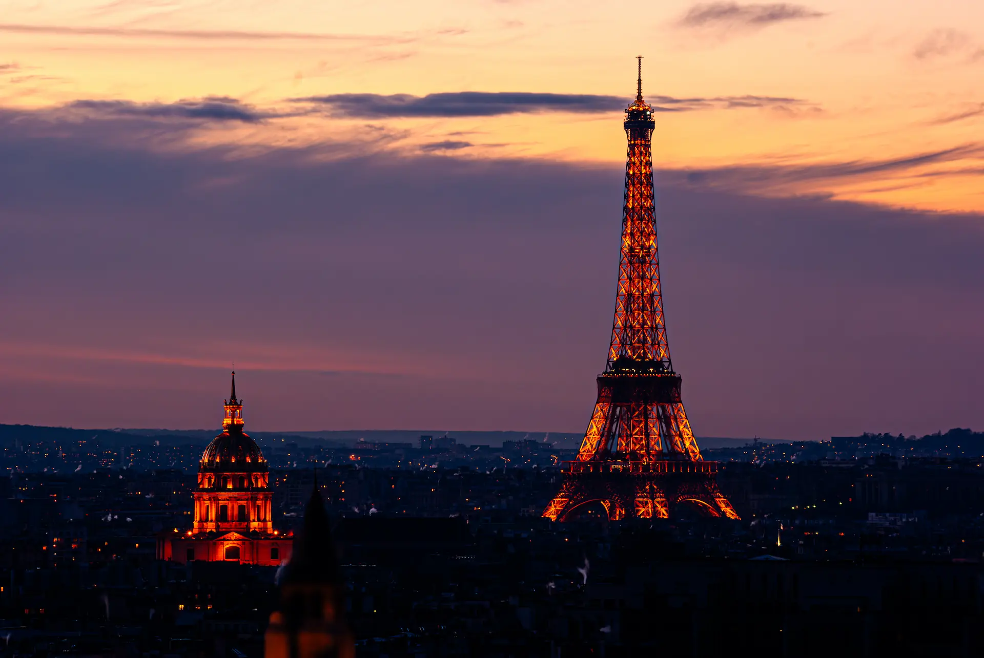 A stunning photograph of the Eiffel Tower and the dome of Les Invalides in Paris, illuminated against a vibrant twilight sky.