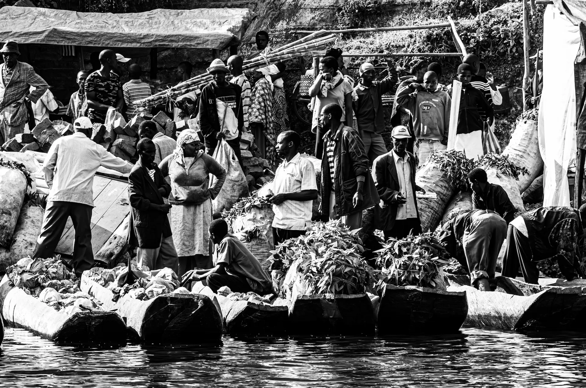 A dynamic black and white photograph capturing a bustling tea market scene on the shores of Lake Bunyonyi in Uganda.