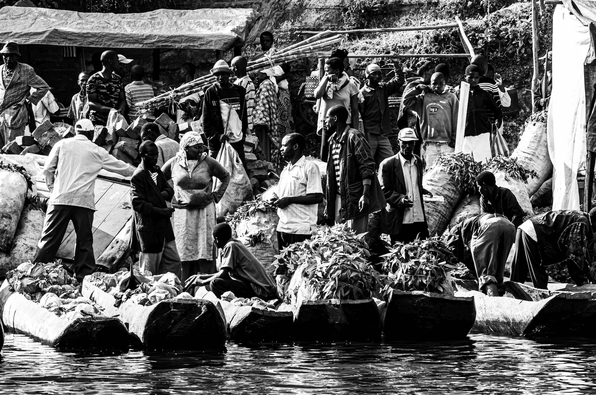A dynamic black and white photograph capturing a bustling tea market scene on the shores of Lake Bunyonyi in Uganda.
