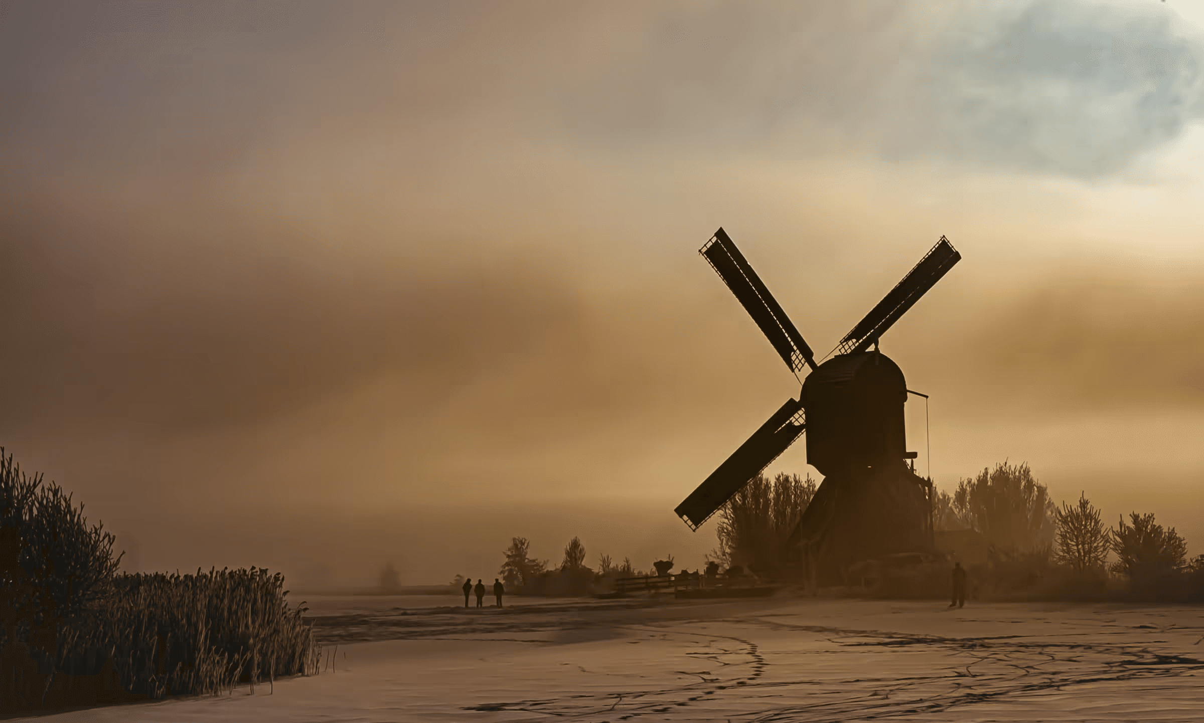 Landscape photograph of a Dutch windmill silhouetted against a misty, golden sky. The windmill's dark form stands prominently on a snowy or frosty field.