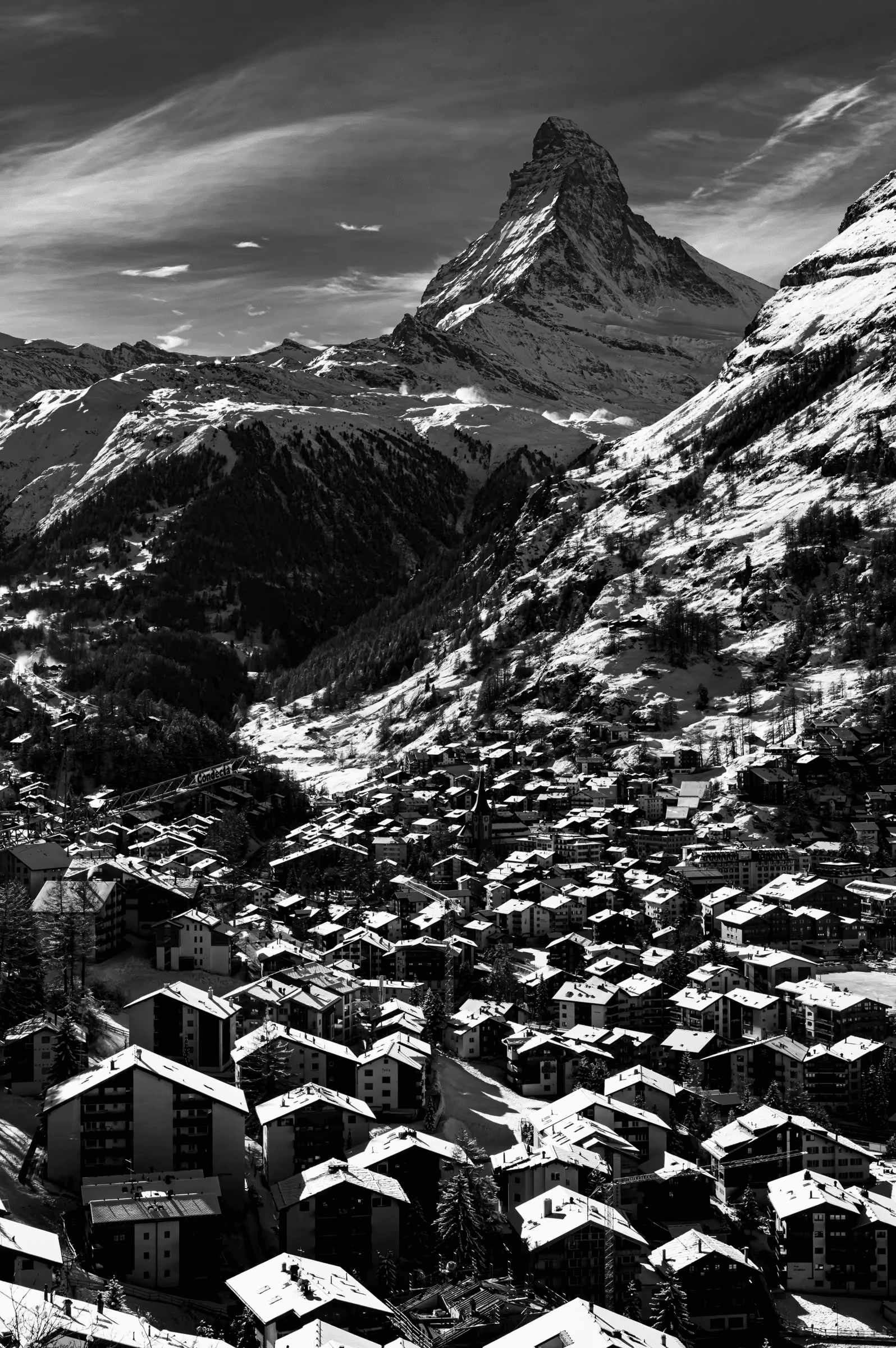 High-contrast, black and white photograph of the snow-covered village of Zermatt, with the iconic Matterhorn mountain in the background.