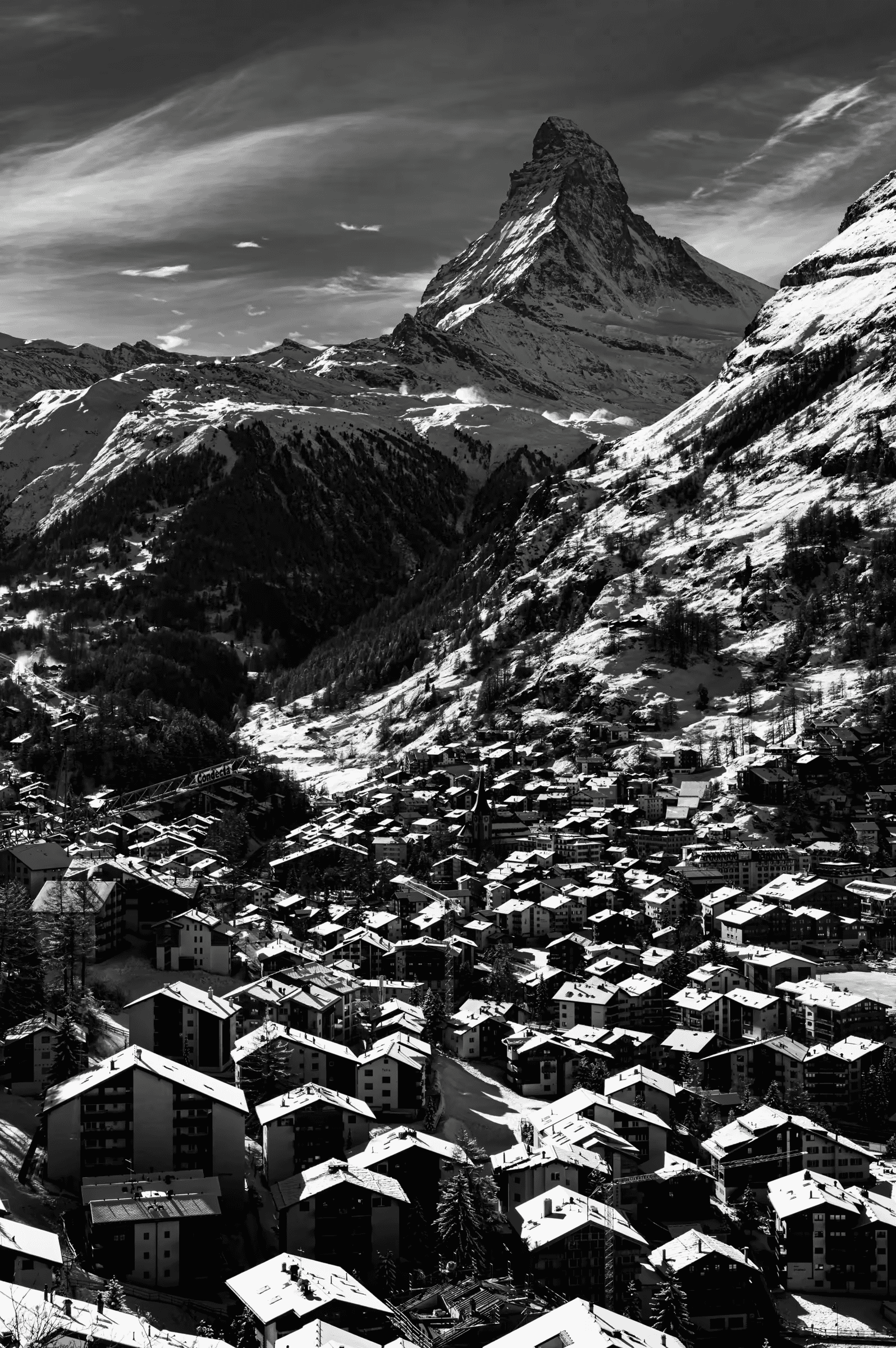 High-contrast, black and white photograph of the snow-covered village of Zermatt, with the iconic Matterhorn mountain in the background.