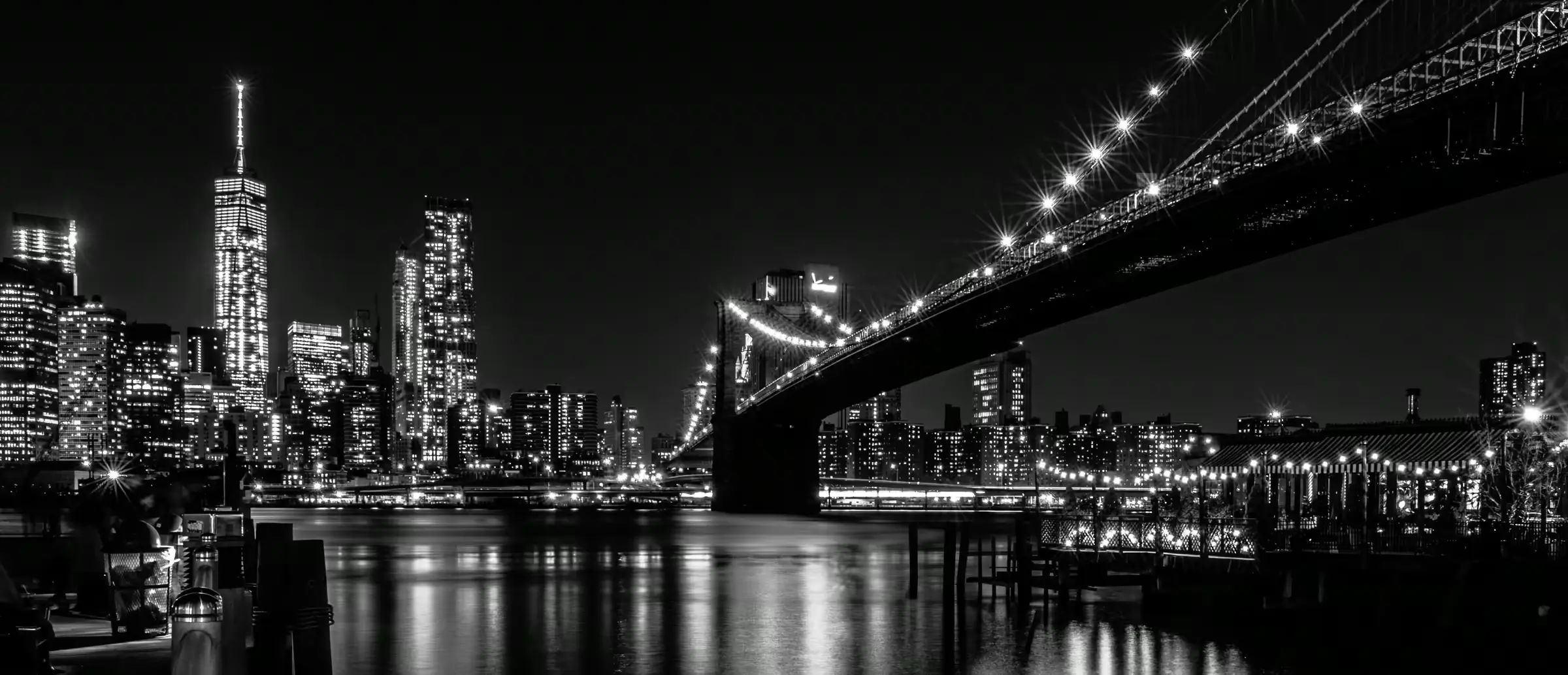Brooklyn Bridge: Urban Nocturne Black-and-white photograph of the Brooklyn Bridge at night, with the lit Manhattan skyline behind it.