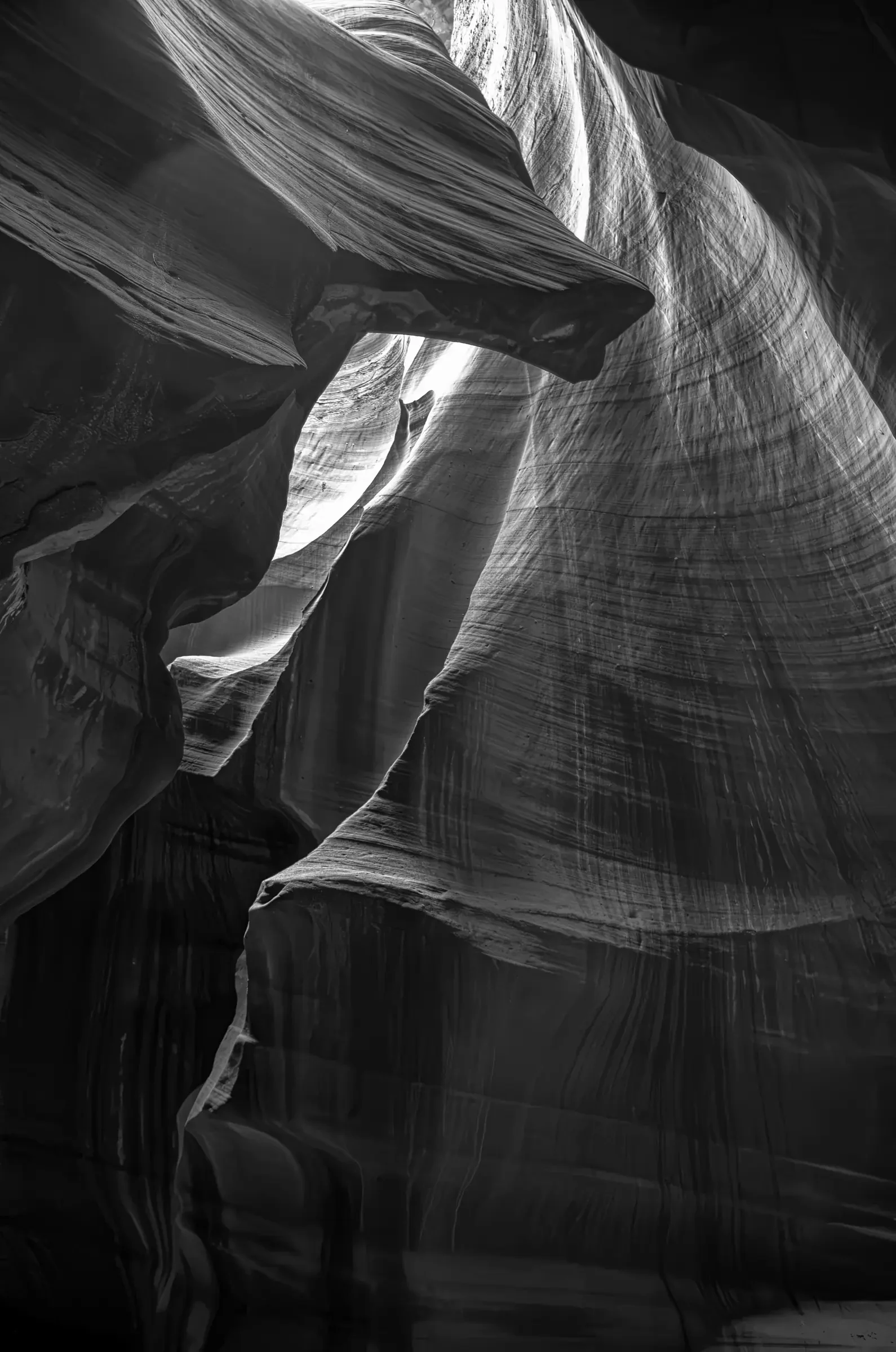 Interior of Antelope Canyon slot canyon showing striated sandstone walls folded around a bright shaft of light, rendered in black-and-white.
