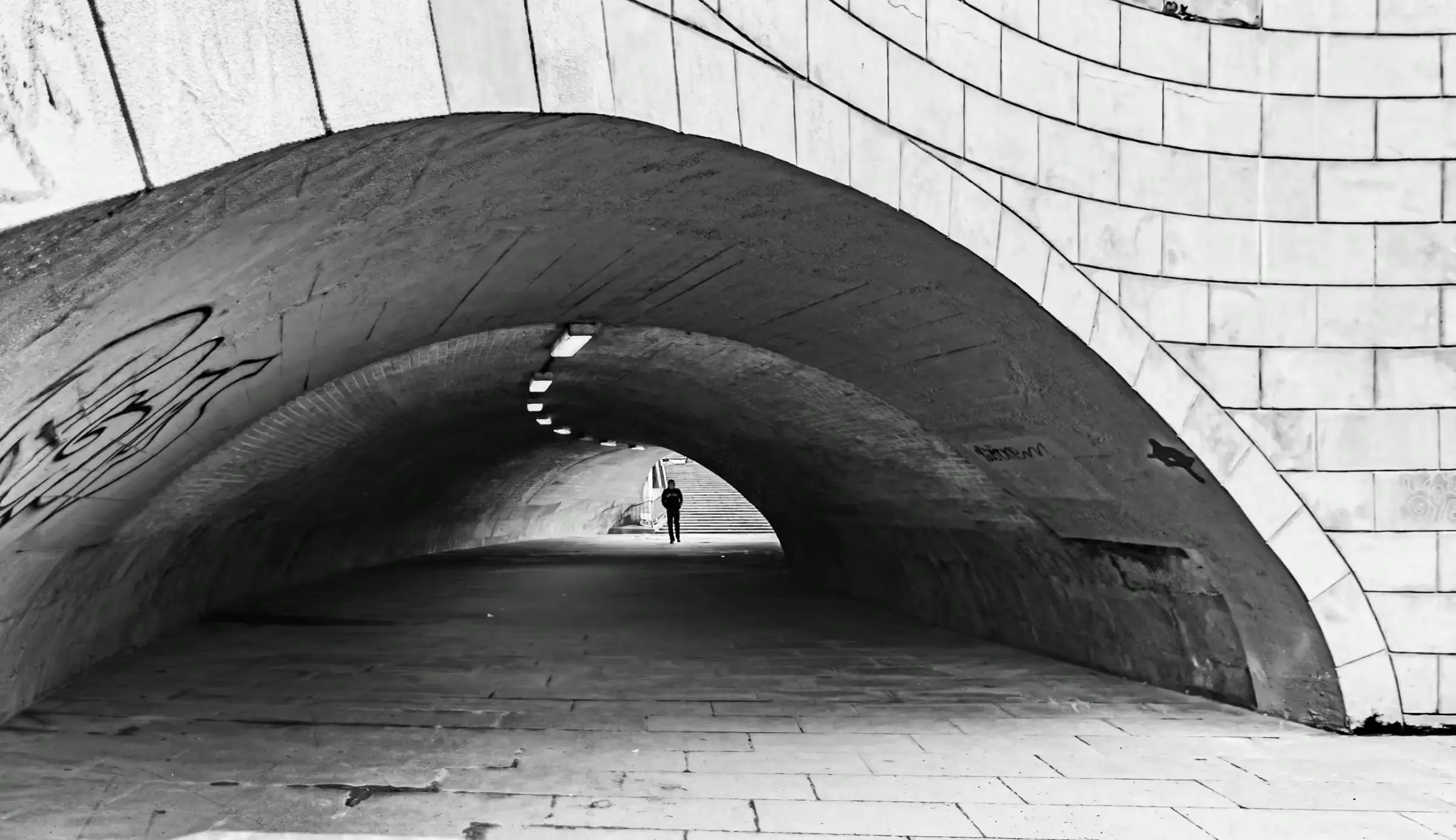 Urban Passageway in Monochrome Black-and-white photograph of a person walking through an arched tunnel in Berlin.