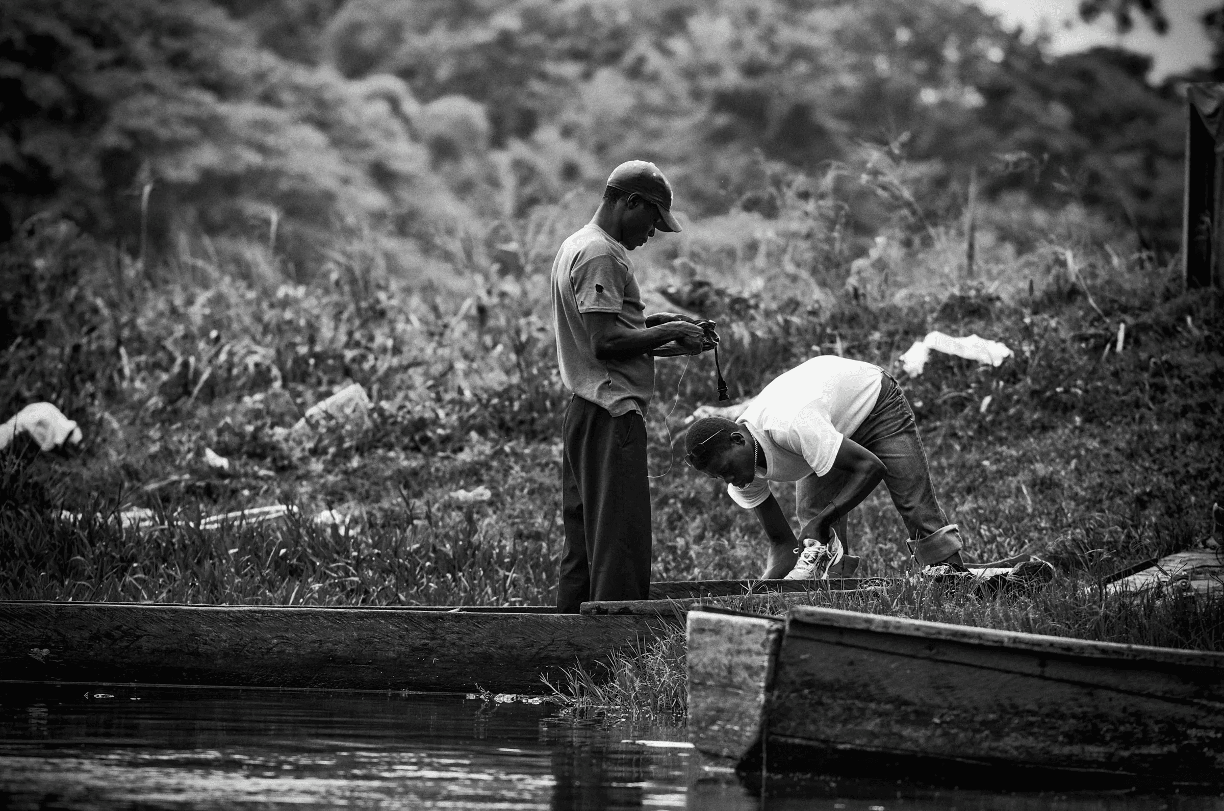 Fishermen's Preparations Two men working on or near simple boats/canoes on a riverbank, possibly preparing fishing gear.