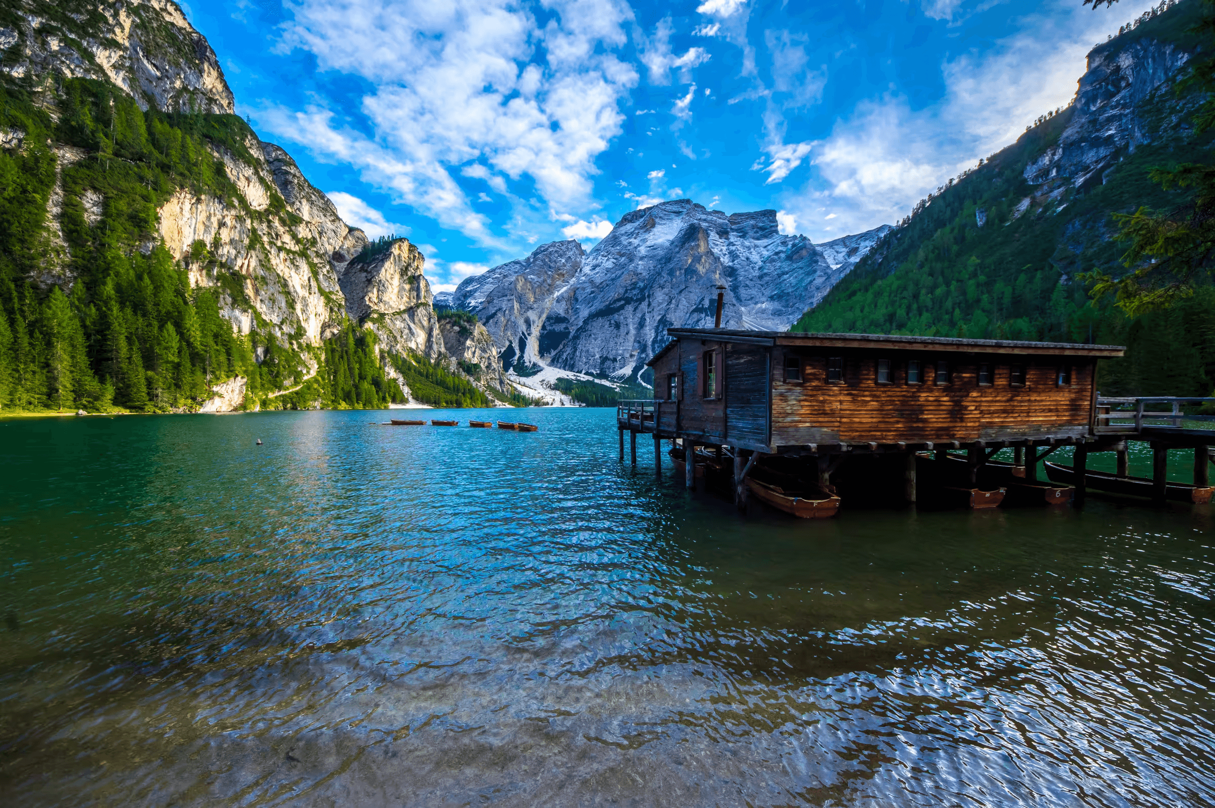 Landscape photograph of Lago di Braies (Pragser Wildsee) in the Dolomites, Italy. A wooden boathouse sits on the edge of the turquoise lake.
