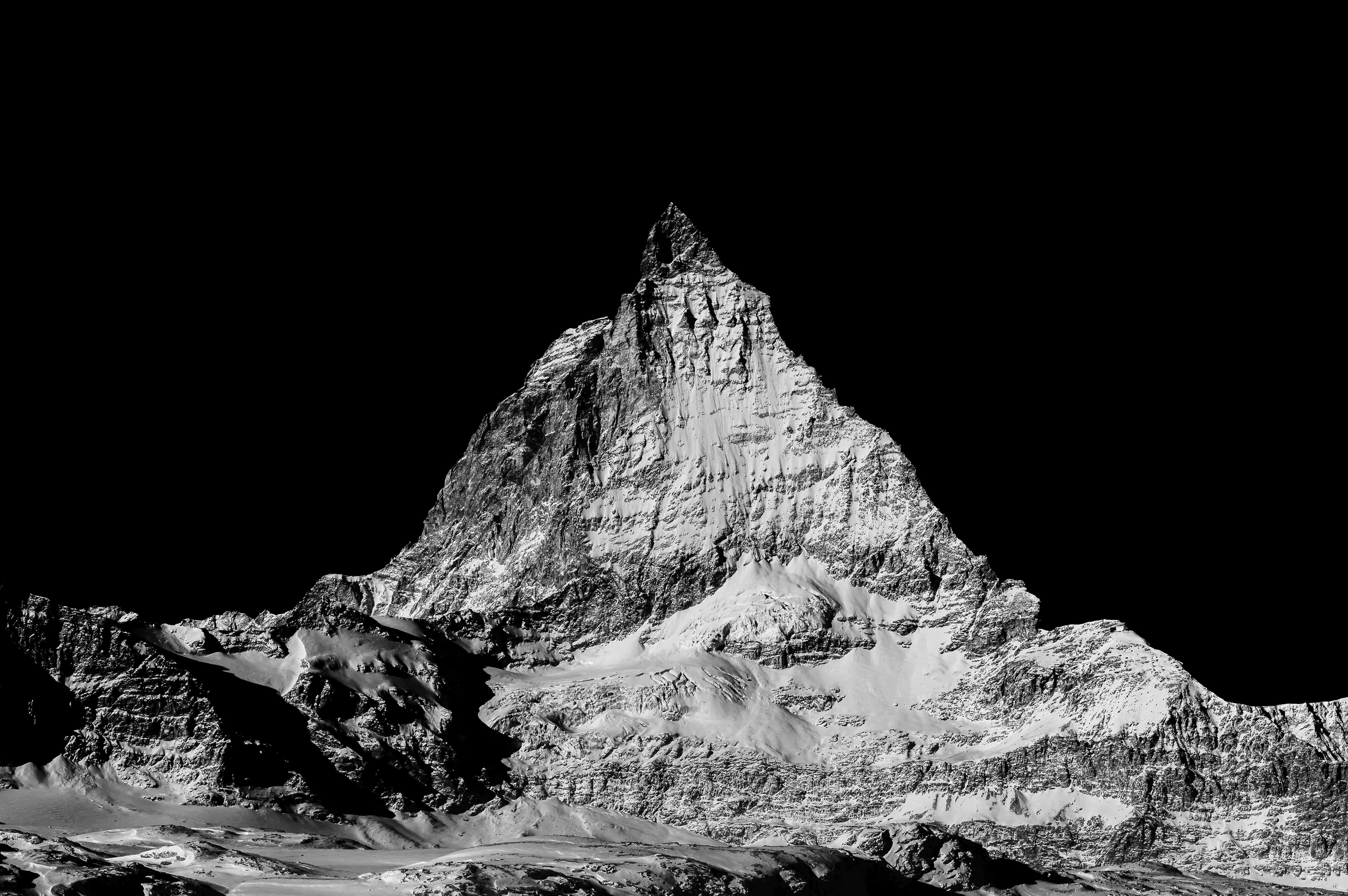 Matterhorn in Stark Relief Black-and-white photograph of the Matterhorn mountain with sharp contrast against a deep black sky, highlighting the rugged textures and snow-covered slopes.