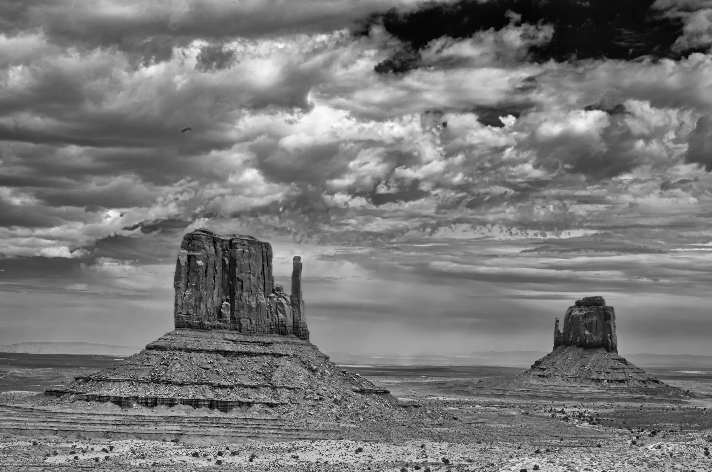 Two large sandstone buttes rise from a flat desert plain beneath a dramatic, cloud-filled sky.