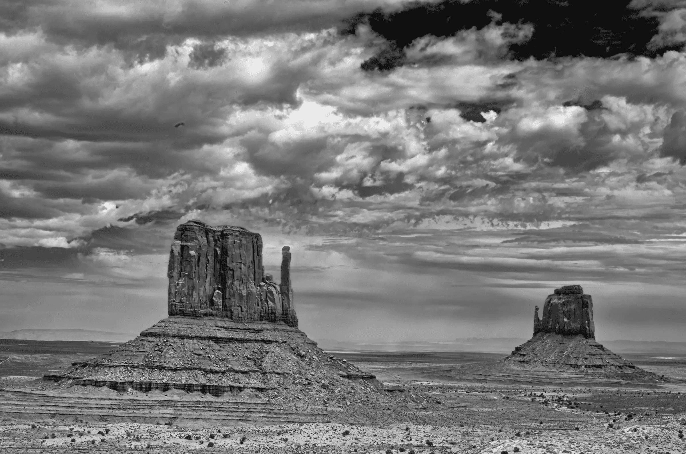 Monuments Under Weather Two large sandstone buttes rise from a flat desert plain beneath a dramatic, cloud-filled sky.