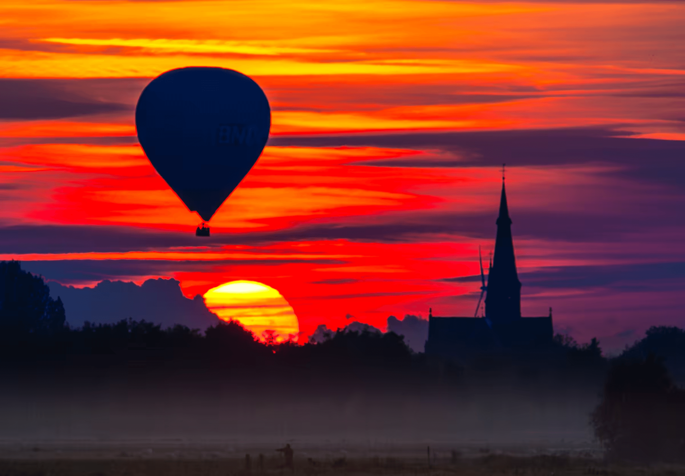 Landscape photograph of a hot air balloon silhouetted against a vibrant sunset in North Brabant, Netherlands.