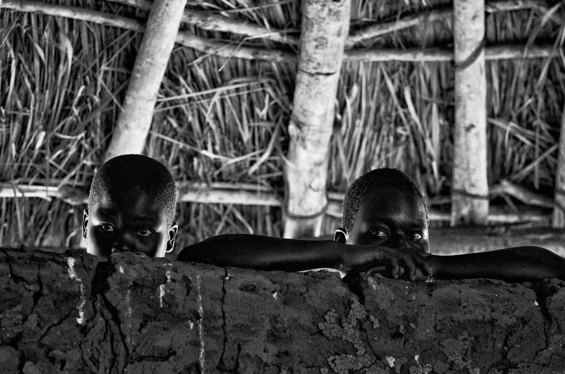 Black-and-white photograph of children peering over a wall in North Uganda.