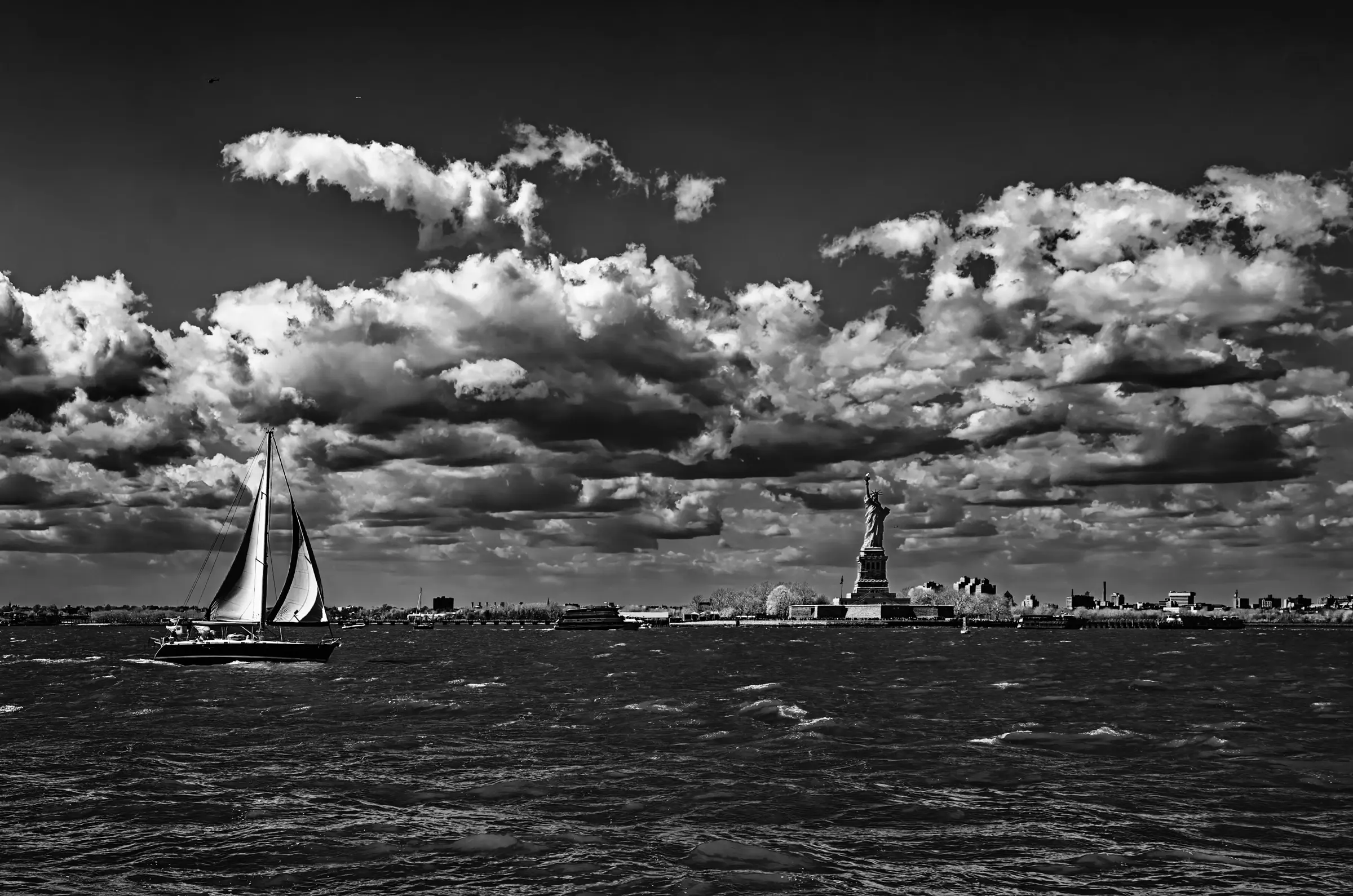 Cityscape with Sailboat Black-and-white photograph of a sailboat in New York Harbor with the Statue of Liberty.