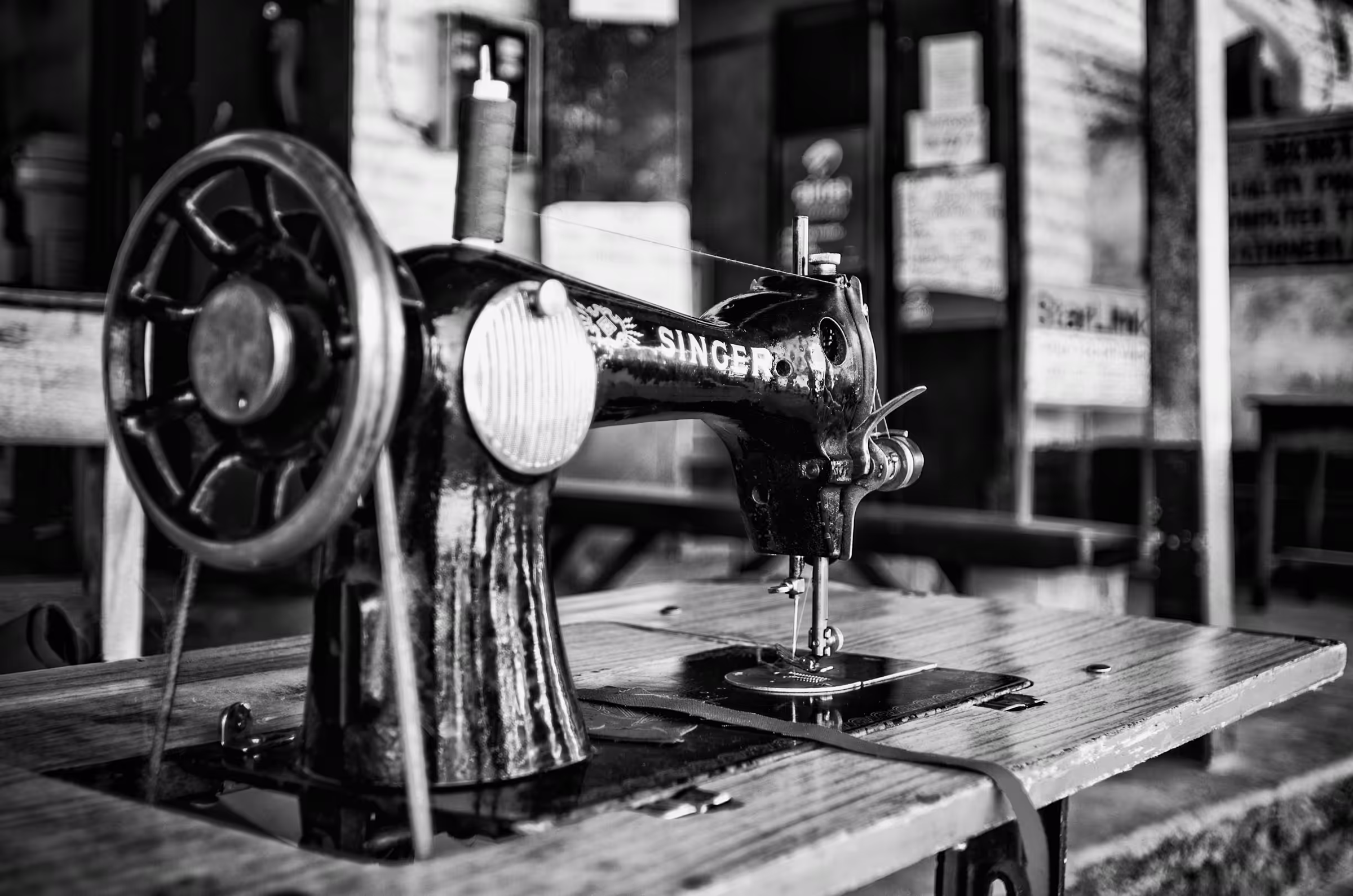 Black and white photograph of a vintage Singer sewing machine in Botswana. The machine, prominently displaying the 'SINGER' logo, sits on a wooden table.
