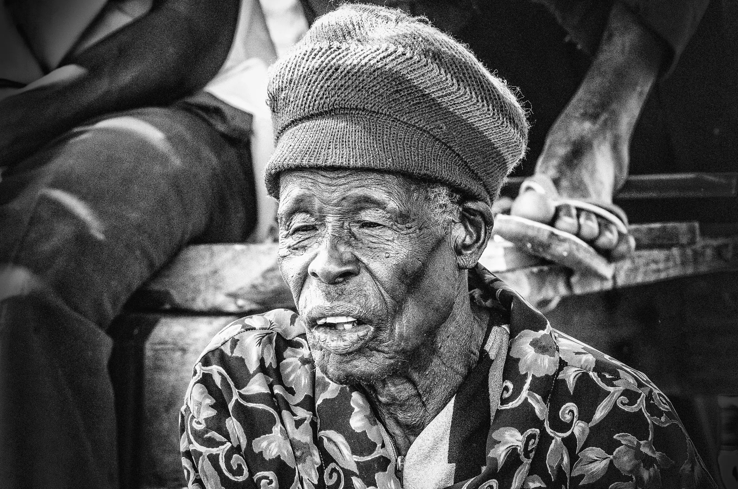Quiet Witness, Uganda Black-and-white close portrait of an older man wearing a knit cap and patterned jacket in Uganda.