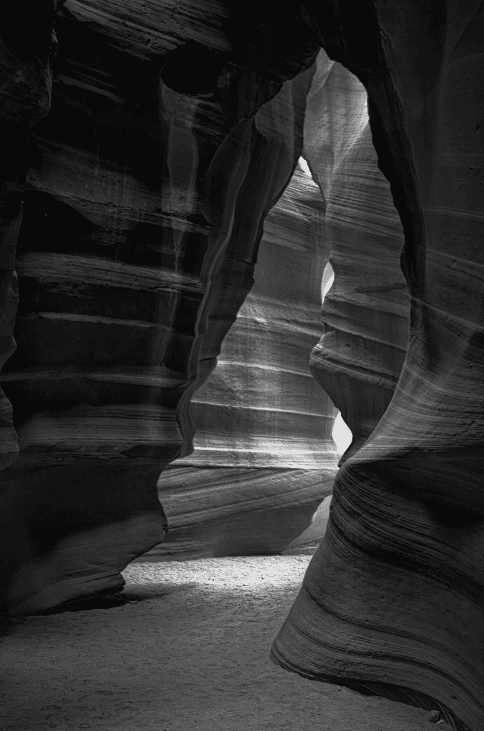 Monochrome layered view of sculpted sandstone walls and a light-filled passage in Antelope Canyon, Arizona.