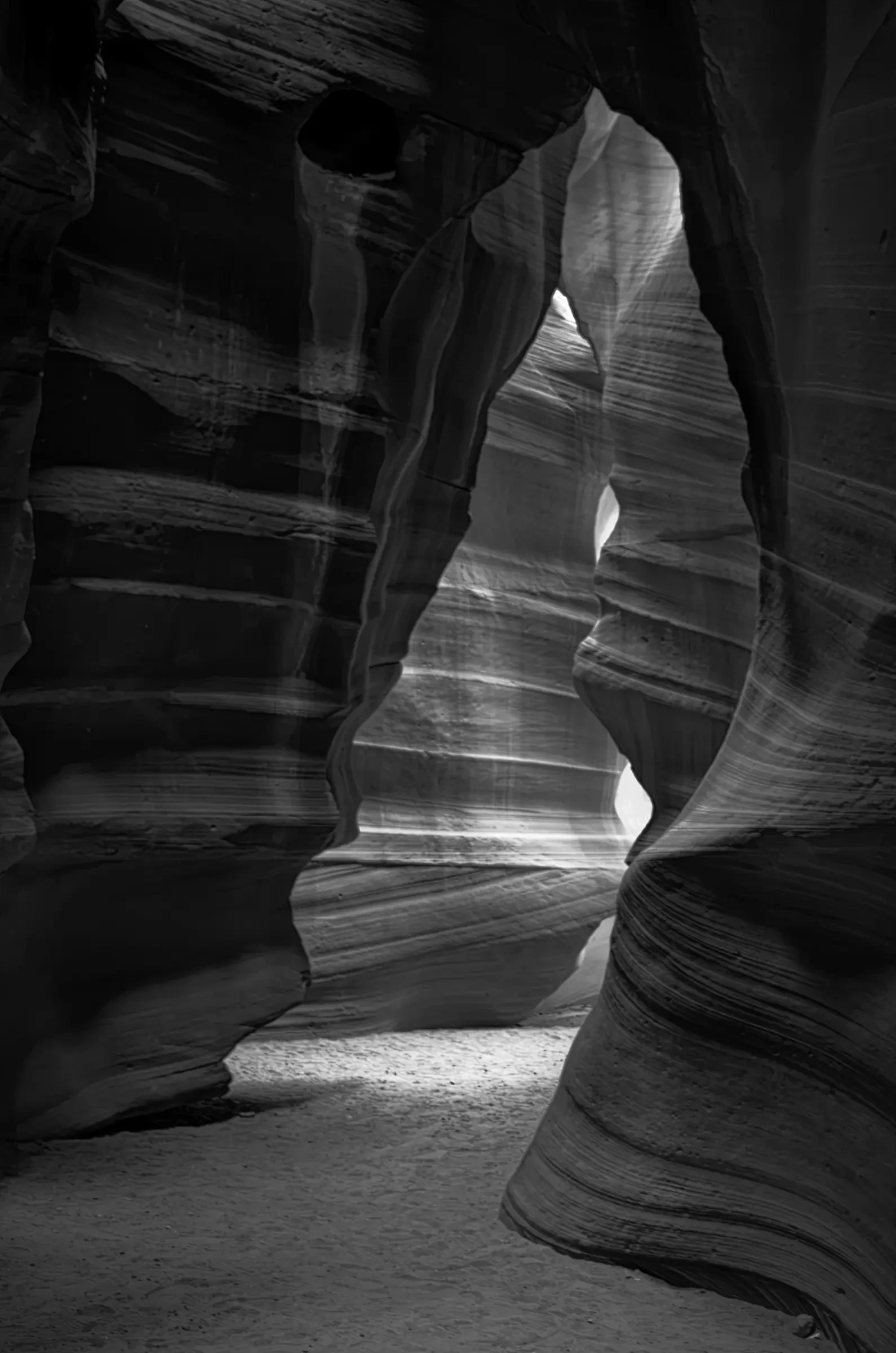 Monochrome layered view of sculpted sandstone walls and a light-filled passage in Antelope Canyon, Arizona.