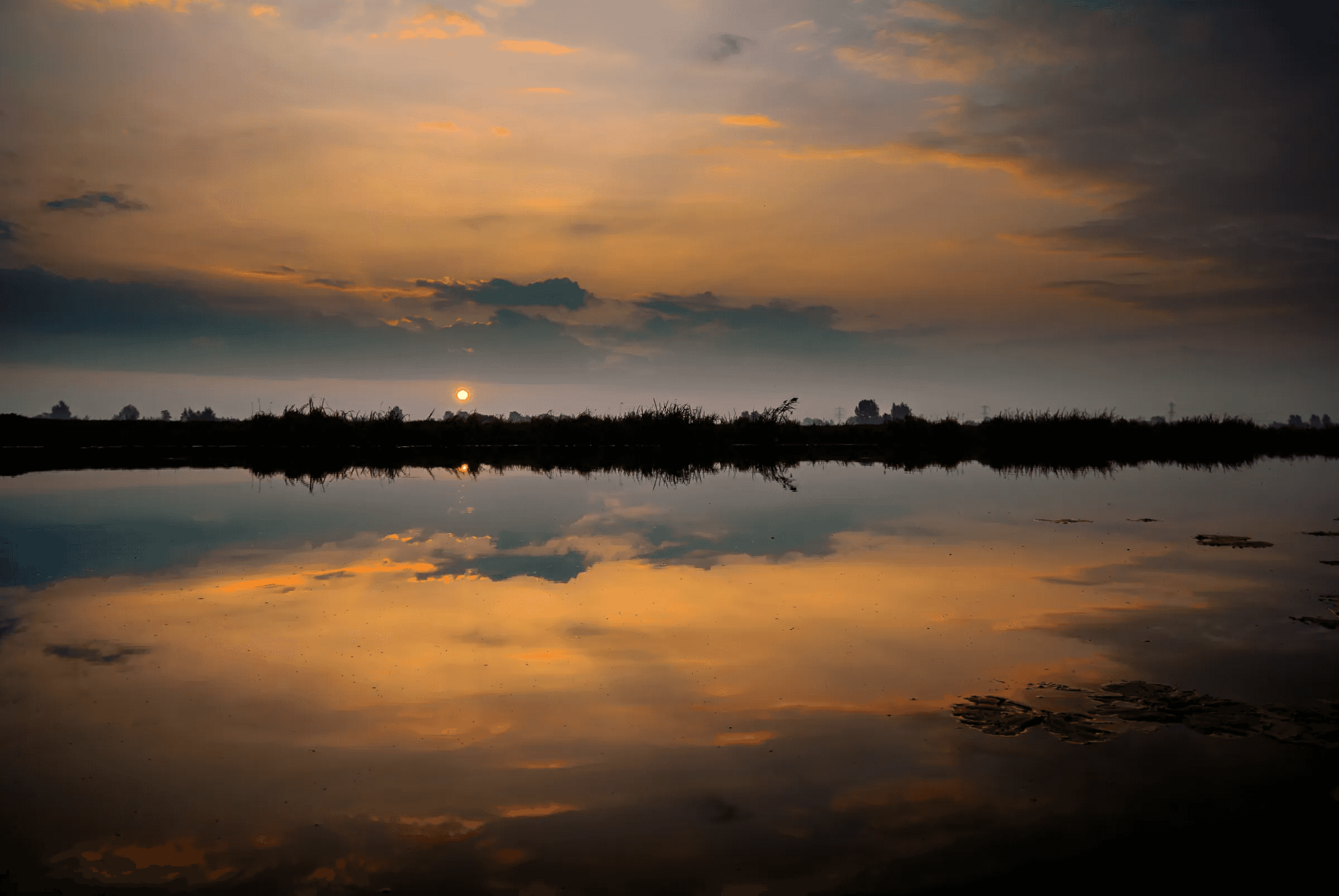 Sunset Reflection Over Calm Waters Vibrant sunset sky with orange and dark clouds reflected in calm water.