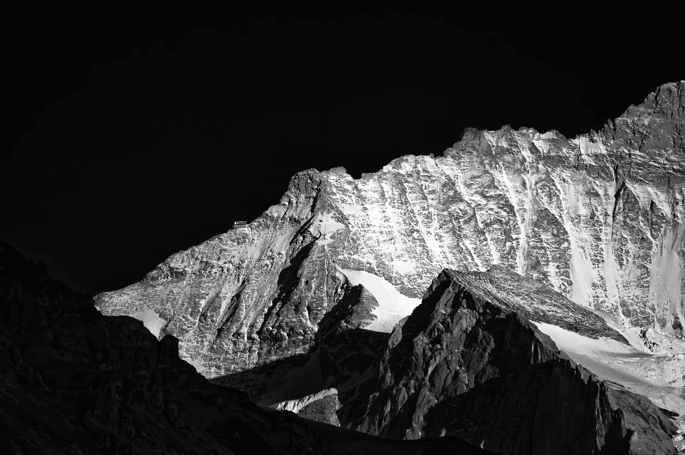 High-contrast black and white study of snow-dusted Swiss Alps peaks against a dark sky.