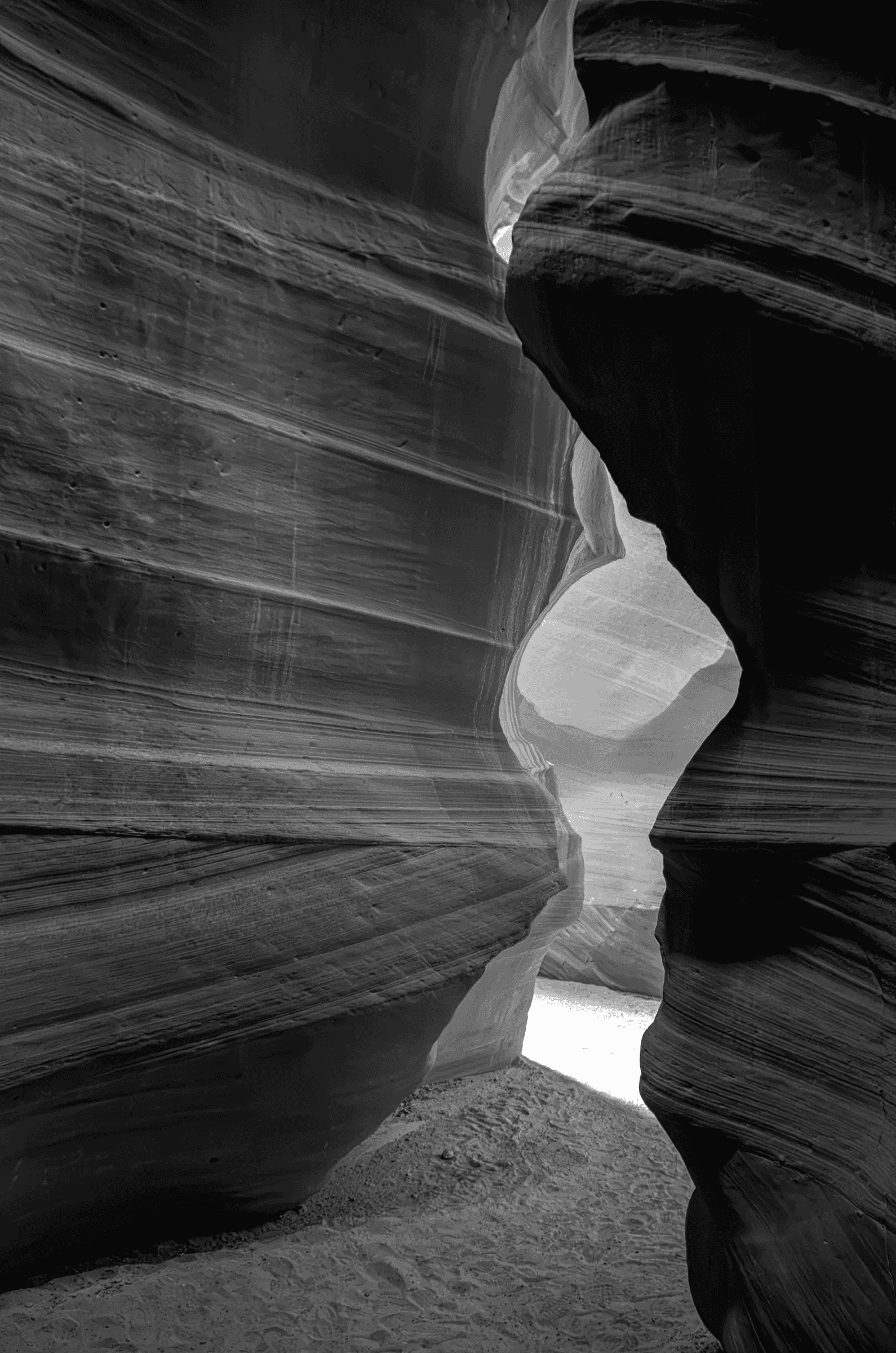 Black-and-white view through the curved, layered sandstone walls of Antelope Canyon in Arizona, with daylight entering through a narrow opening.