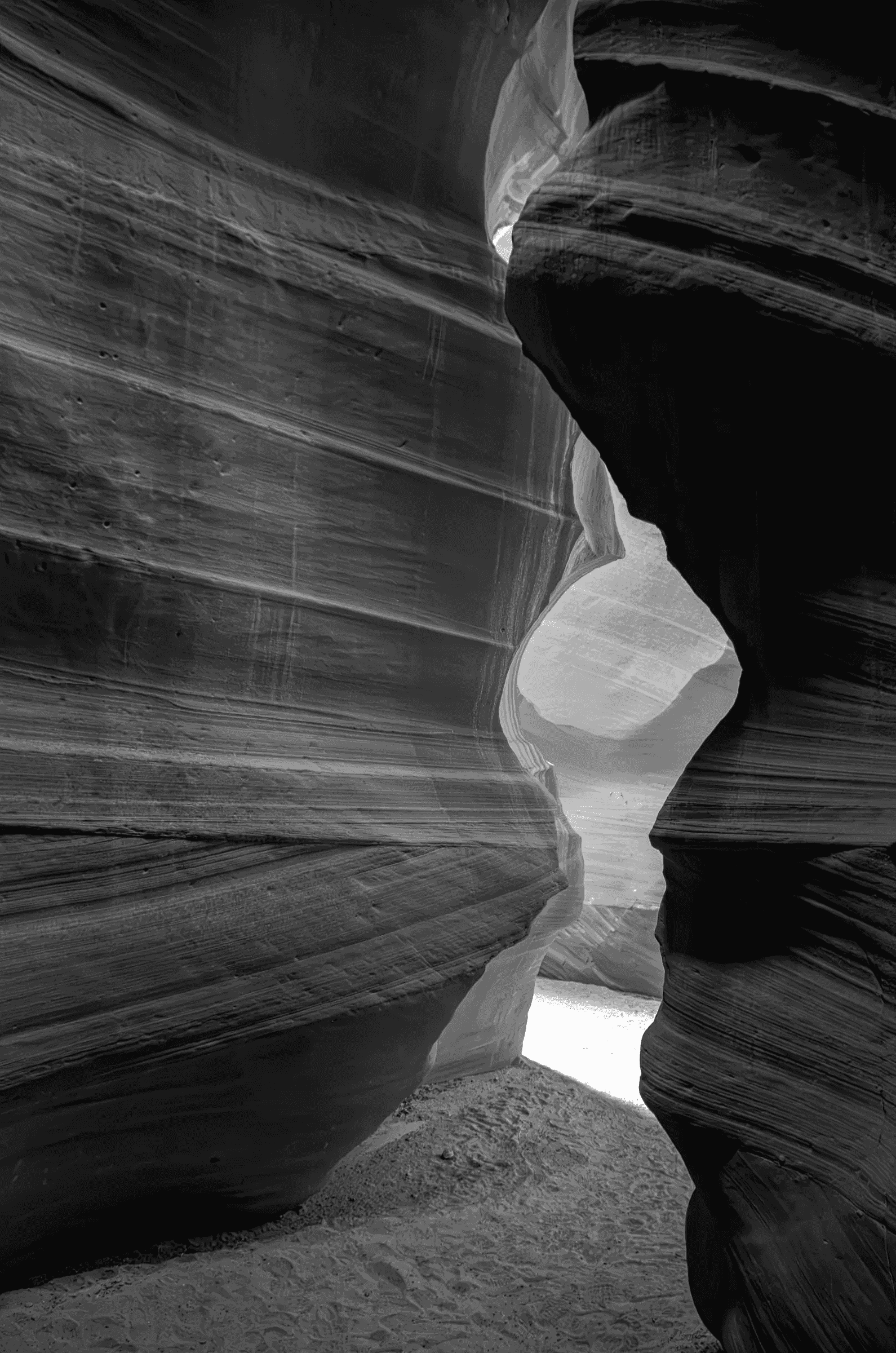 The Long Passage Black-and-white view through the curved, layered sandstone walls of Antelope Canyon in Arizona, with daylight entering through a narrow opening.