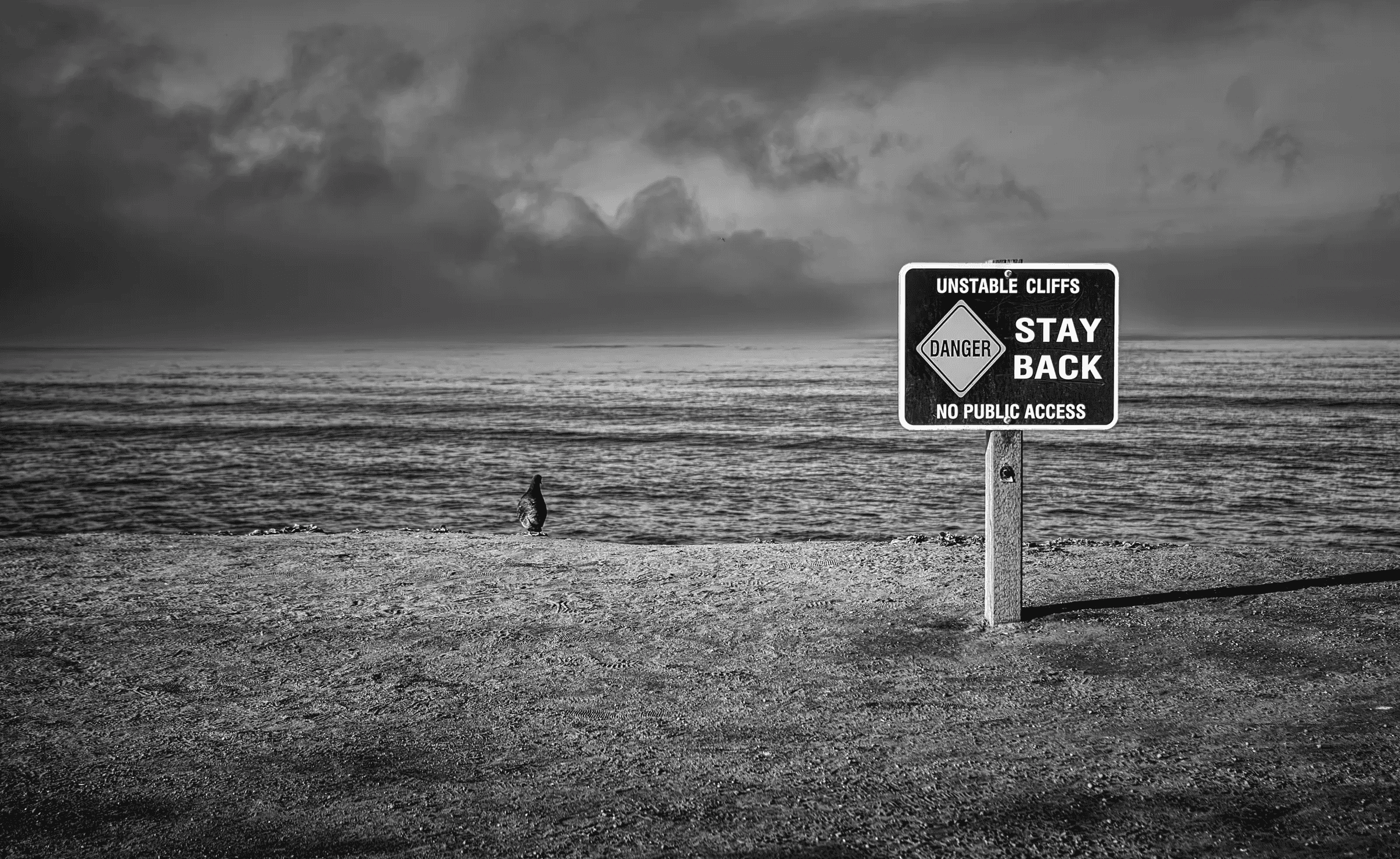 Unstable Cliffs Warning Landscape view of unstable cliffs warning sign coast in monochrome.