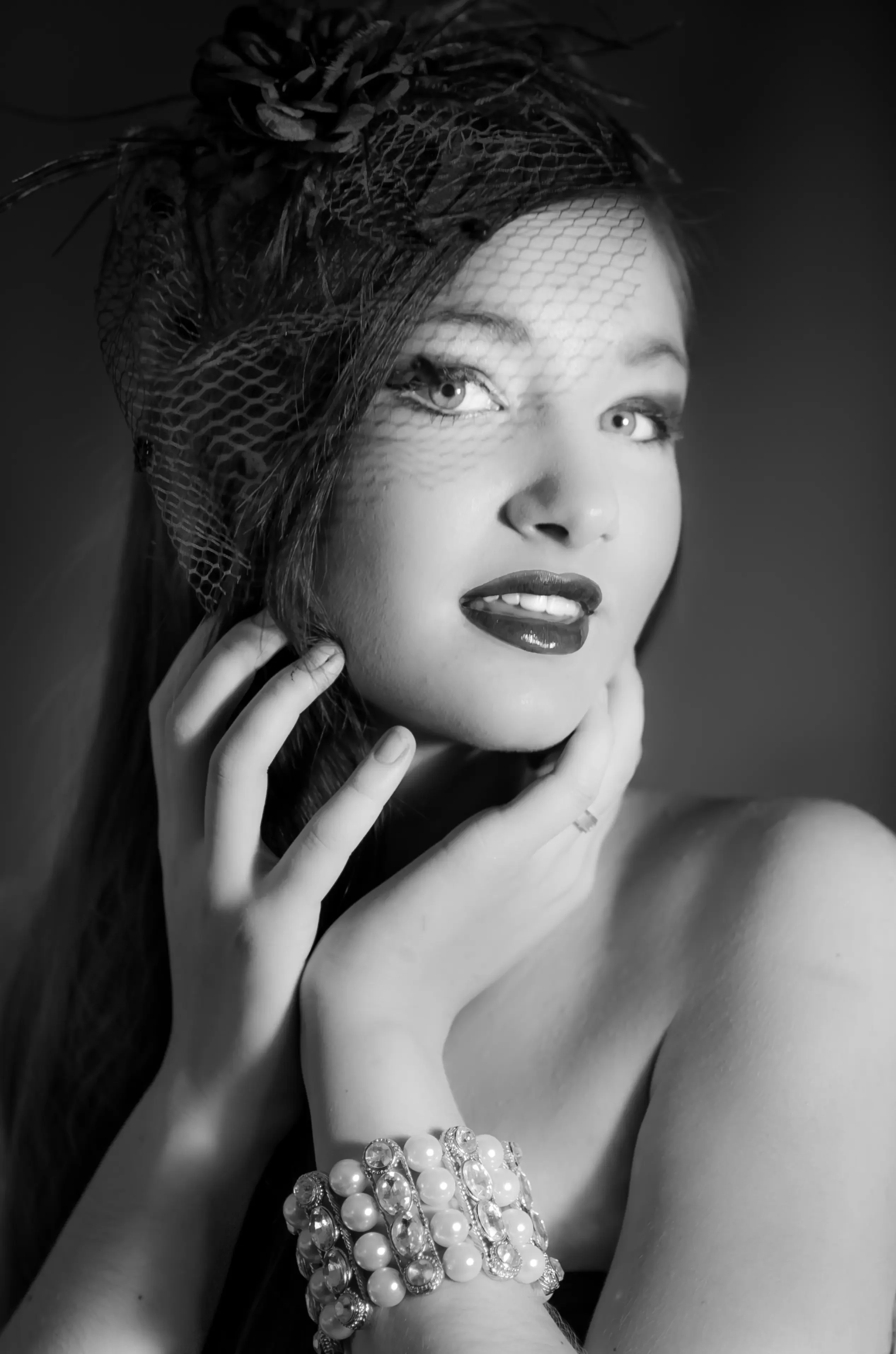 Black and white portrait of a woman wearing a vintage-style veiled headpiece and a pearl bracelet.